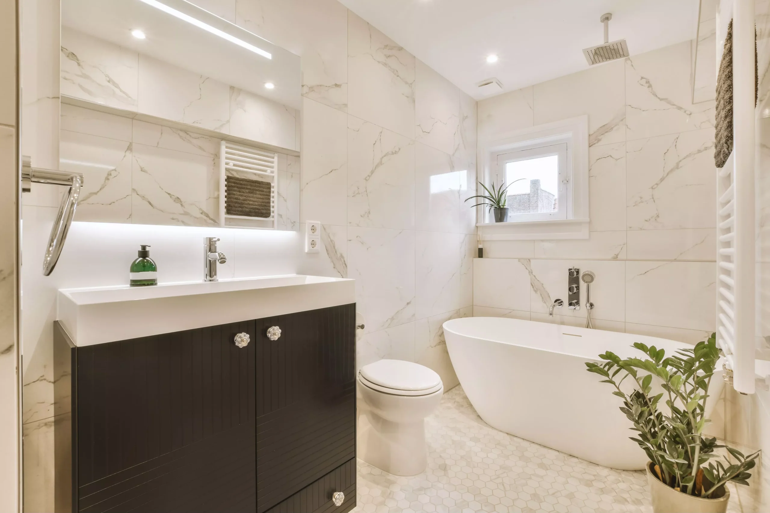 Elegant modern bathroom with white marble-tiled walls, dark brown vanity, sink, mirror, freestanding tub, and green plants. Elegant modern bathroom with white marble-tiled walls, dark brown vanity, sink, mirror, freestanding tub, and green plants.